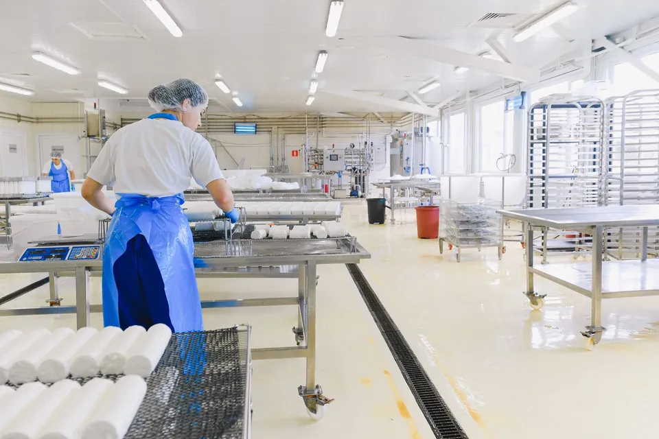 Operaria con cofia y delantal azul trabajando en una planta de alimentos limpia e iluminada