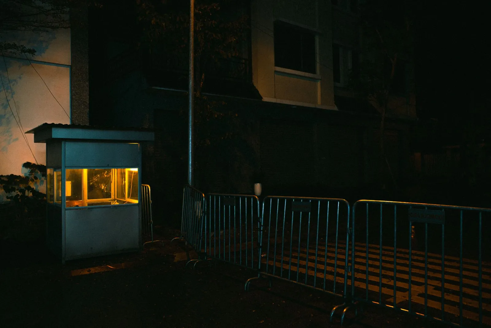Garita de guardia iluminada de noche junto a una reja en un recinto oscuro
