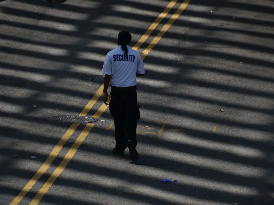 Guardia de seguridad caminando por una calle vista desde arriba, entre franjas de luz y sombra